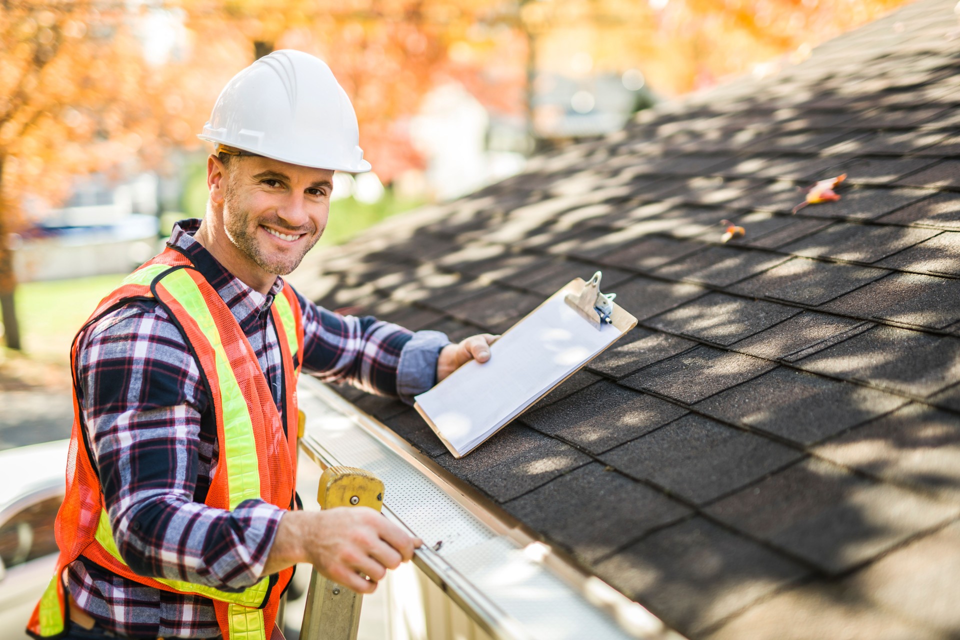 man with hard hat standing on steps inspecting house roof